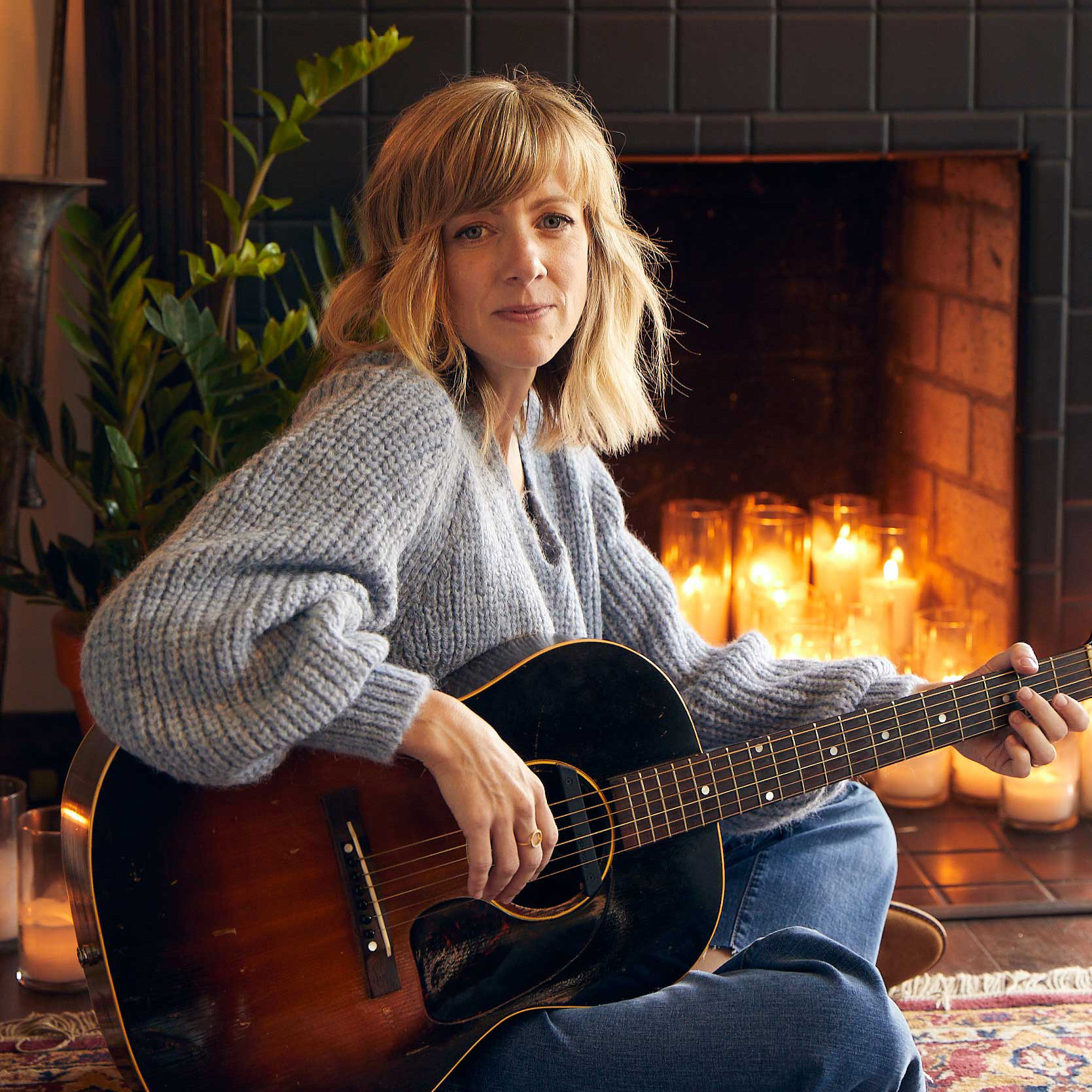 Sandra McCracken at a fireplace with a guitar